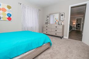 Shreveport apartment for rent - A cypress bedroom with a teal bedspread and a white dresser with mirror at The Marq in Shreveport, LA