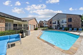 Denton apartment for rent - A pool with comfortable lounge chairs and a bench at The Oaks of Denton Apartments in Denton, TX
