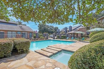Shreveport apartment for rent - A swimming pool surrounded by a stone patio and green bushes.