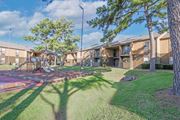 Shreveport apartment for rent - A playground with a slide and a tree in front of apartment buildings at Stone Canyon apartments in Shreveport, LA.