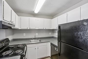 Norcross apartment for rent - A black refrigerator is in the corner of a kitchen with white cabinets.