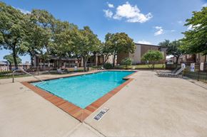 Euless apartment for rent - A large outdoor swimming pool surrounded by trees and a building in the background.
