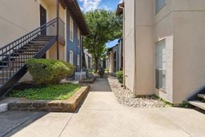 Dallas apartment for rent - A yellow apartment building exterior and paved walkway at Windridge on the Parkway in Dallas, TX