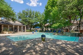 Plano apartment for rent - A swimming pool surrounded by trees and the leasing office in the background at La Costa Apartments in Plano, TX