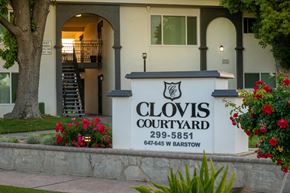 Clovis apartment for rent - The entrance to Clovis Courtyard with a sign and flowers.