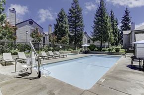 Fresno apartment for rent - A swimming pool surrounded by lounge chairs and trees.