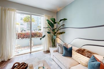 Miami apartment for rent - A living room with a couch, a plant, and a view of a balcony with chairs and a table.