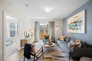 Methuen apartment for rent - A living room with a grey couch, a wooden chair, and a painting on the wall.