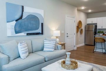 Pensacola apartment for rent - A living room with a grey couch and a painting on the wall.