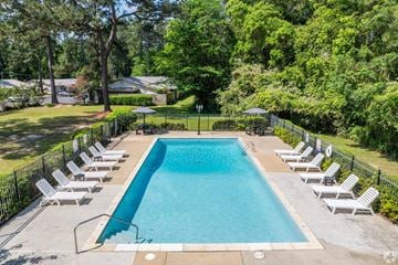 Thomasville apartment for rent - A large swimming pool surrounded by white lounge chairs and green trees.