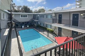 Houston apartment for rent - A pool surrounded by a black fence and red umbrellas.