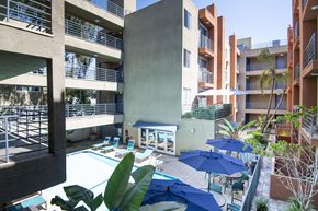 Los Angeles apartment for rent - A pool area with blue umbrellas and chairs is surrounded by apartment buildings.