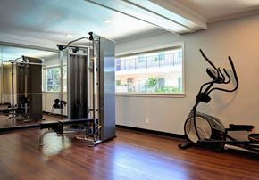 Sherman Oaks apartment for rent - Community gym featuring elliptical and weight machine with wood look flooring and well lit window