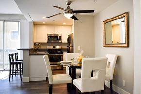 Los Angeles apartment for rent - View of model kitchen and dining area with white cabinets, stainless appliances, dark counters, wood look flooring, bar on other side of counter, and dining table and chairs