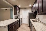 Folsom apartment for rent - View into kitchen with stone counters, tile back splash, stainless appliances, and brown cabinets