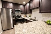 Sacramento apartment for rent - View of kitchen with stone counters, inlaid sink, stainless appliances, tile backsplash, brown cabinets, and wood look flooring.