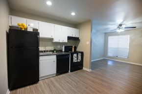 Huntsville apartment for rent - View of kitchen at Rolling Brook with wood look flooring, black appliances, dark counters, white cabinets, recessed lighting, and well lit window in living area