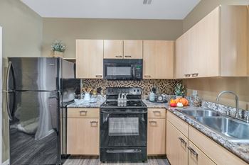 A kitchen with wood cabinets and black appliances and a stainless steel refrigerator