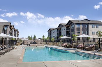 A swimming pool surrounded by lounge chairs and umbrellas in front of apartment buildings