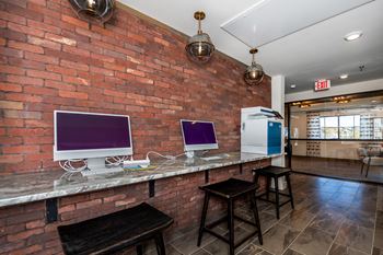 A room with a brick wall and a bar area with two computers on it
