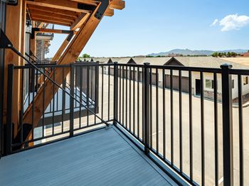 A wooden deck with a metal railing and a staircase leading to a balcony