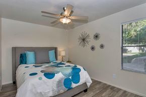Mesa apartment for rent - A bedroom with a bed, pillows, a ceiling fan, and a window with blinds at Reflections at Red Mountain Apartments, Arizona