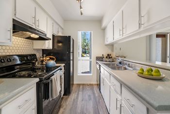 A kitchen with white cabinets and black appliances and a window