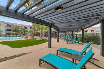A group of blue lounge chairs under awning next to a pool