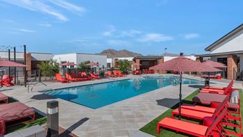A swimming pool with red chairs and umbrellas in front of a building