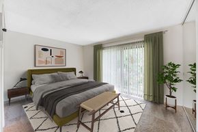 Goleta apartment for rent - Goleta, CA Apartments Near UCSB - Encina Meadows - Spacious Bedroom with Carpeted Flooring, Large Bed, Footboard Bench, Wooden Nightstands with Lamps, Houseplant, White Walls, and Large Window with Green Curtains.