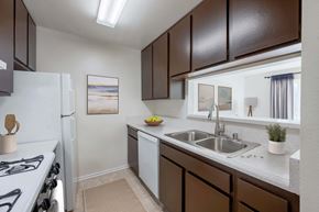 Lompoc apartment for rent - Lompoc, CA, Apartments Near Vandenberg Air Force Base - Oceanwood Apartments - Kitchen Features Dark Wood Cabinets, Sink, And White Appliances.