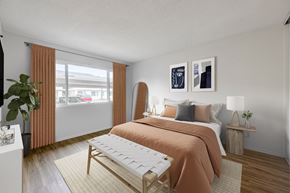 Goleta apartment for rent - Goleta, CA, Apartments Near Target - Pacific Oaks - Bedroom with Wood-Style Flooring, a Bed, an Ottoman, Two Bedside Tables with Lamps, and a Large Window with Curtains.