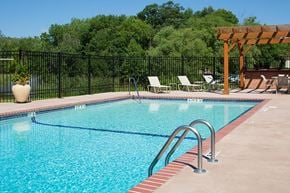 Hopkins apartment for rent - Outdoor pool surrounded by pool chairs and a fence, trees is the background