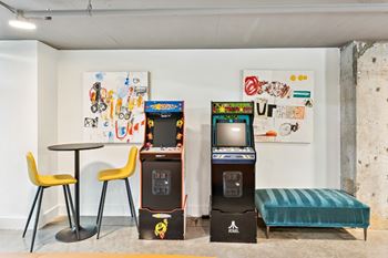 A room with a table, two chairs, a sofa, and two arcade machines