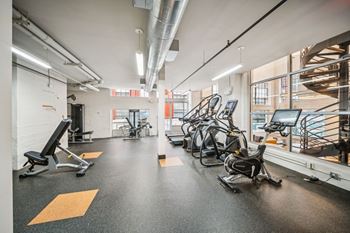 A gym with a variety of exercise equipment including treadmills, stationary bikes, and weight benches