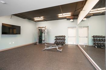 A gym with a mirror, weights, and a television