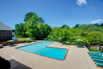 A swimming pool with benches and umbrellas and trees
