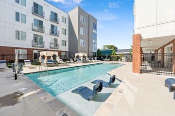 A pool with a slide and sun loungers in front of apartment buildings