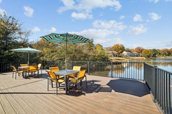 A table with chairs and an umbrella on a wooden deck overlooking a lake