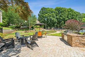 A patio with chairs and a table is surrounded by trees.