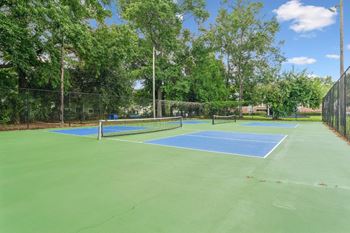 A tennis court surrounded by trees and a fence.
