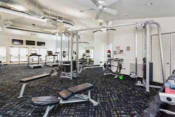 A gym with cardio equipment on the floor and a ceiling fan