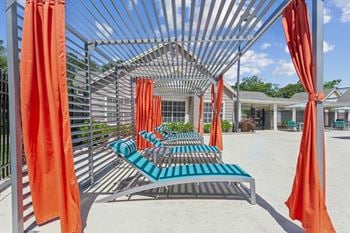 A row of lounge chairs under a metal structure with orange curtains