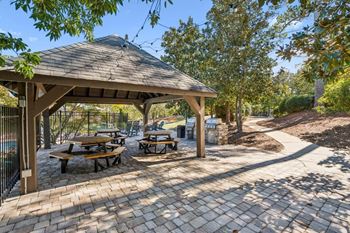 A gazebo with picnic tables is surrounded by trees.