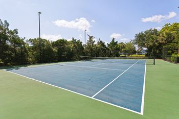 A blue tennis court with green grass and trees