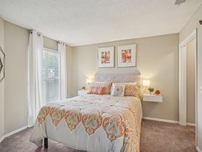 Raleigh apartment for rent - A bedroom with a bed, two pillows, a nightstand, and two framed pictures on the wall at The Falls Apartments in Raleigh NC
