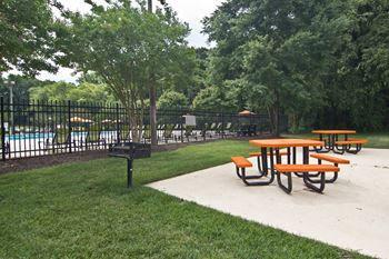 Picnic tables are set up in a park next to a pool.