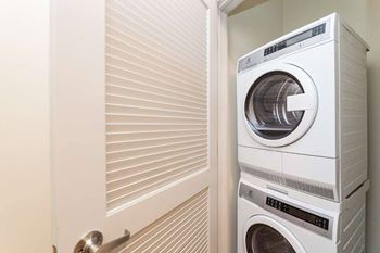 A white washing machine is stacked on top of another in a small laundry room