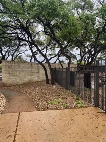 A black fence runs along a sidewalk lined with trees.