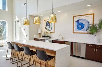 A modern kitchen with a long white island and black chairs.